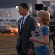 Man and women stand side-by-side with camera in the background. Woman carries a clipboard labeled "NASA"